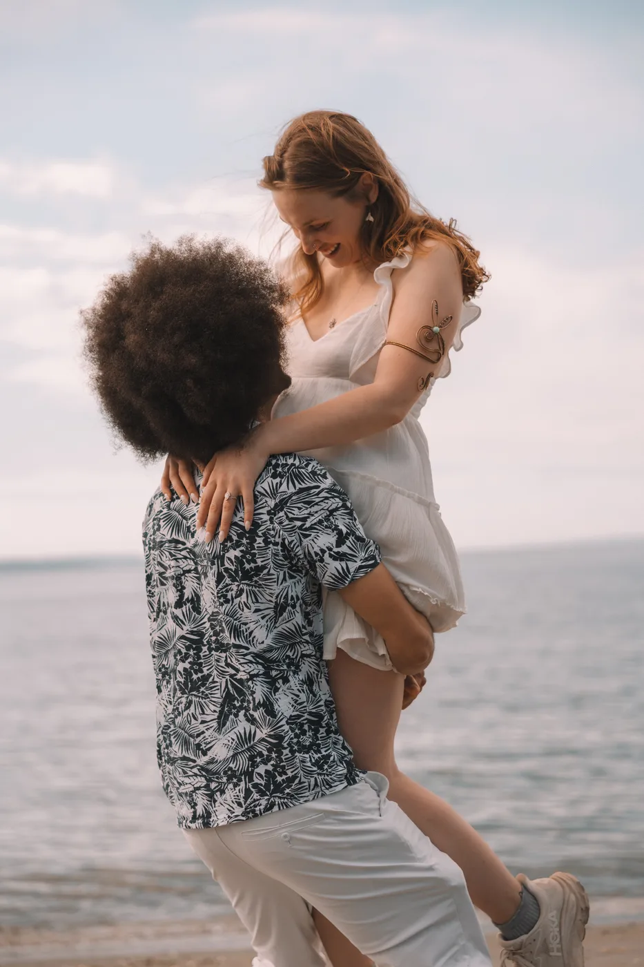 Documentary couple portrait — partner lifting the other in a piggyback embrace on the beach