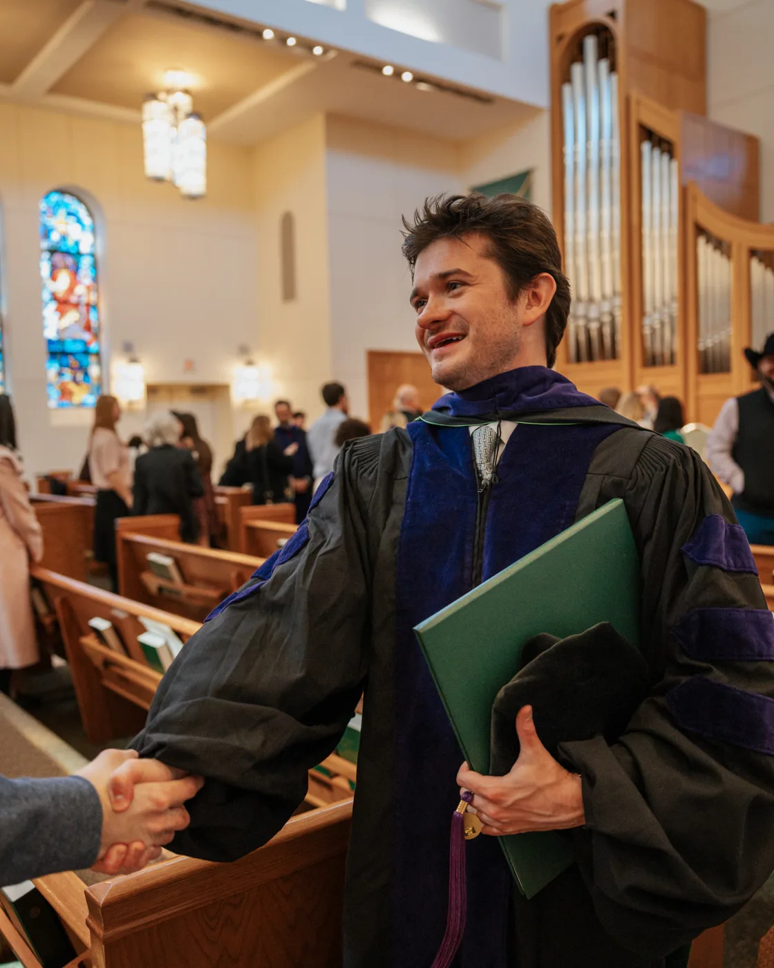 Documentary graduation photography — doctoral graduate shaking hands in a church