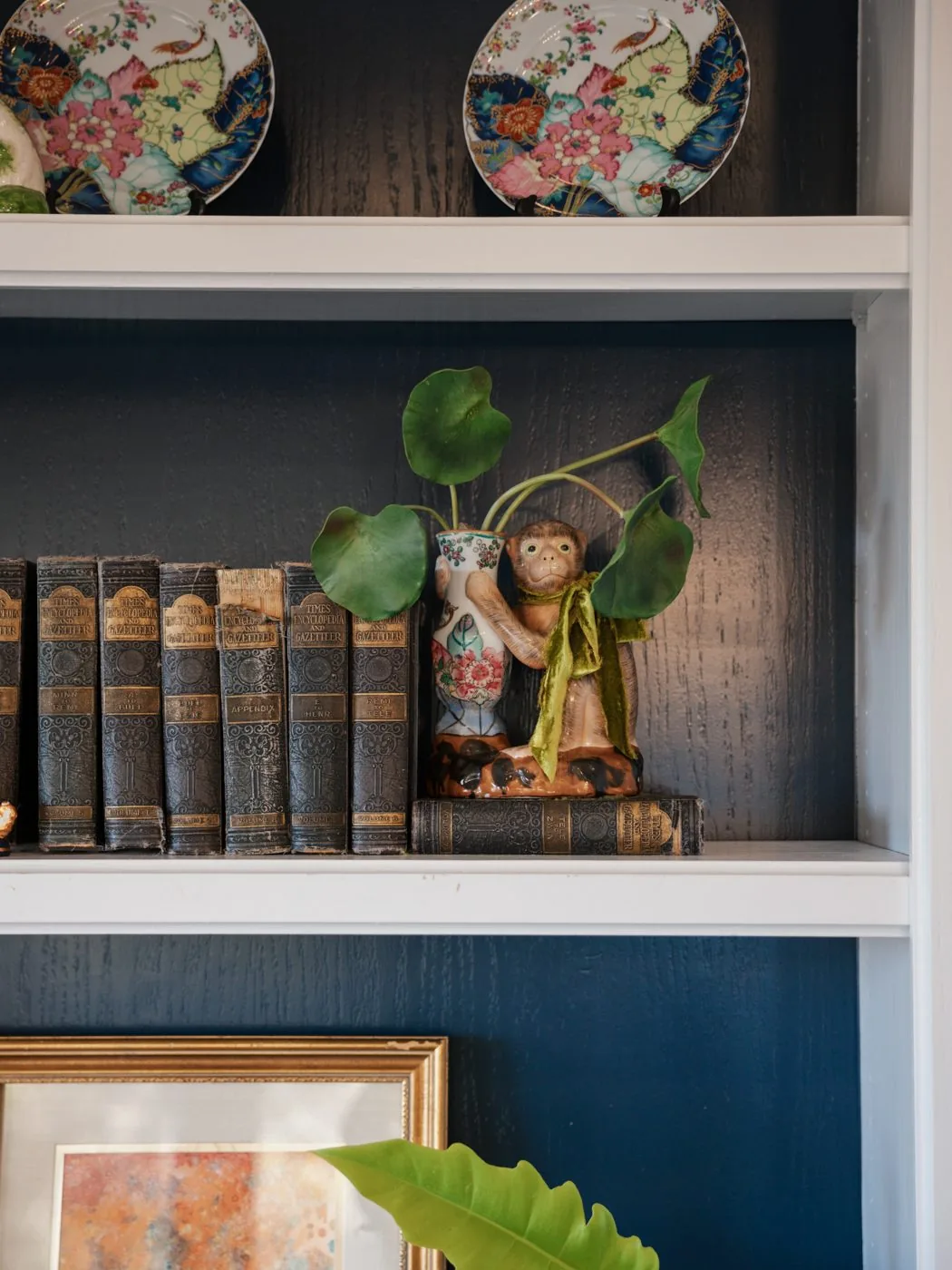 Documentary interior — built-in bookshelf with antique leather-bound books and a ceramic monkey figurine