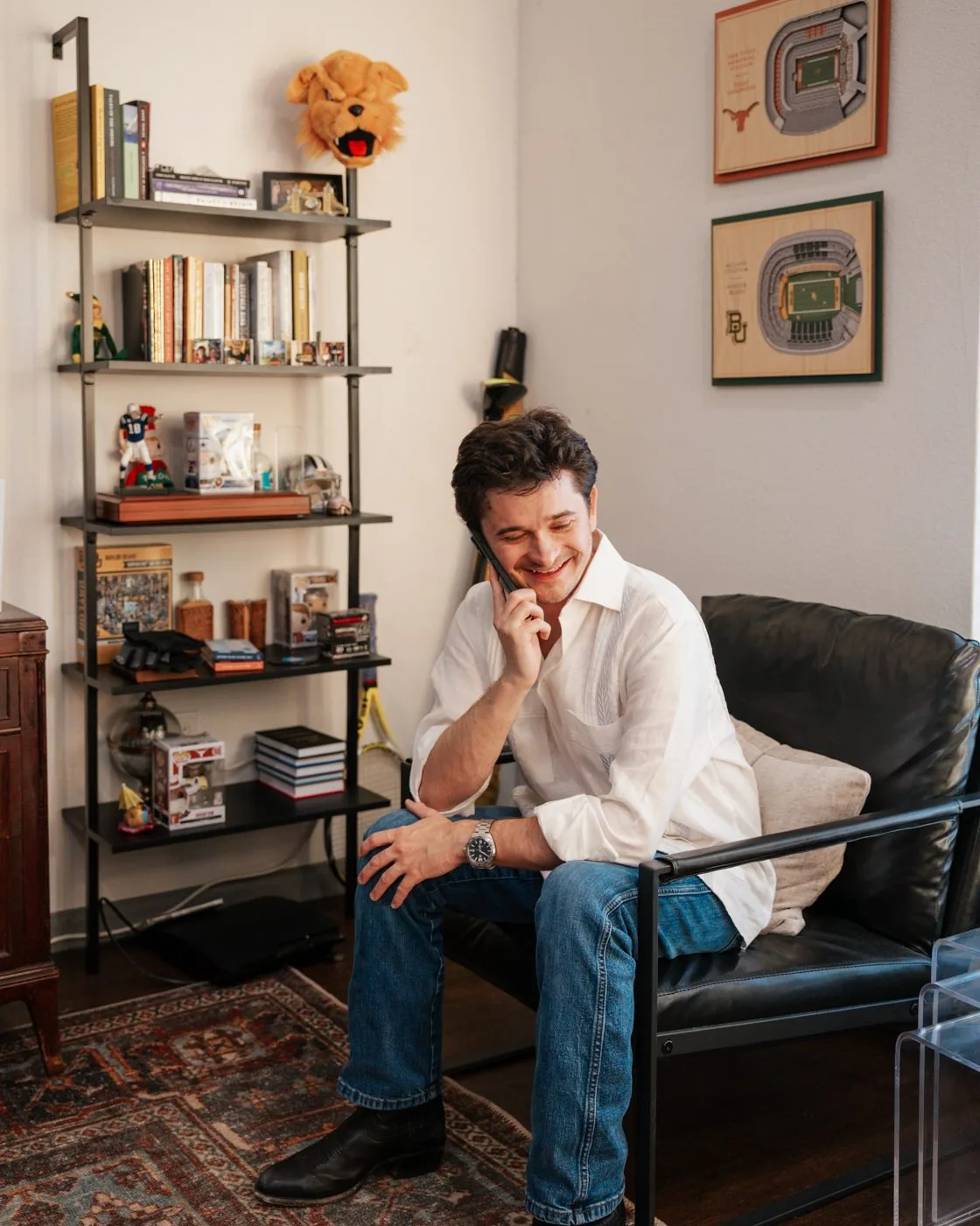 Documentary interior portrait — man laughing on the phone surrounded by books and personal memorabilia