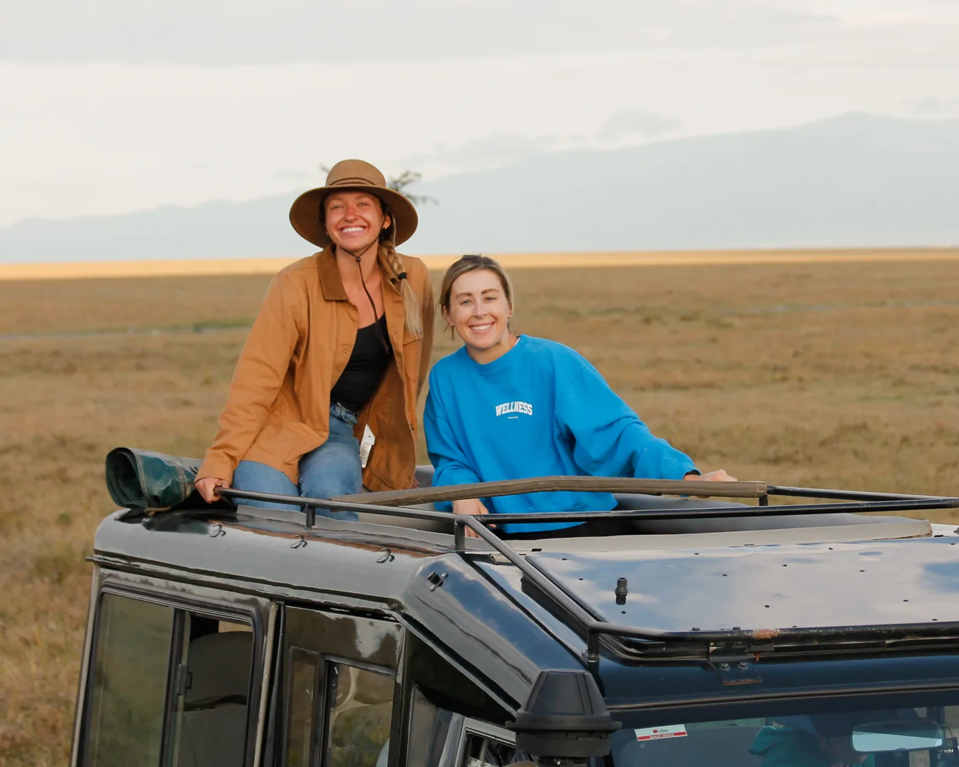 Documentary travel photography — two women standing through the open roof of a safari vehicle on the savanna
